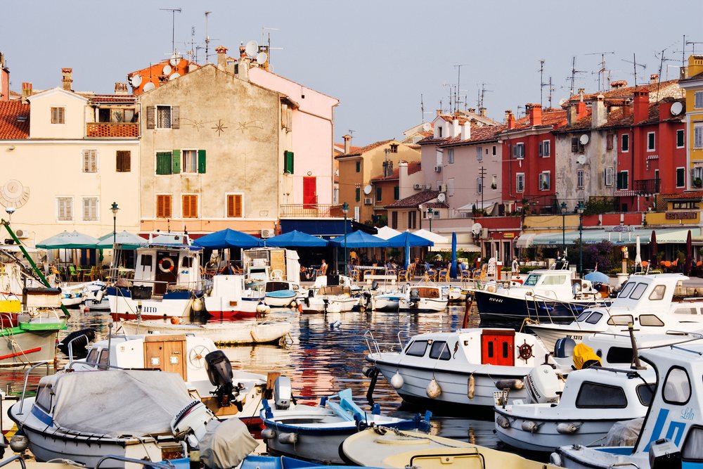 Boats moored peacefully in the harbour of Rovinj, with colorful buildings and outdoor cafes lining the waterfront, Croatia.
