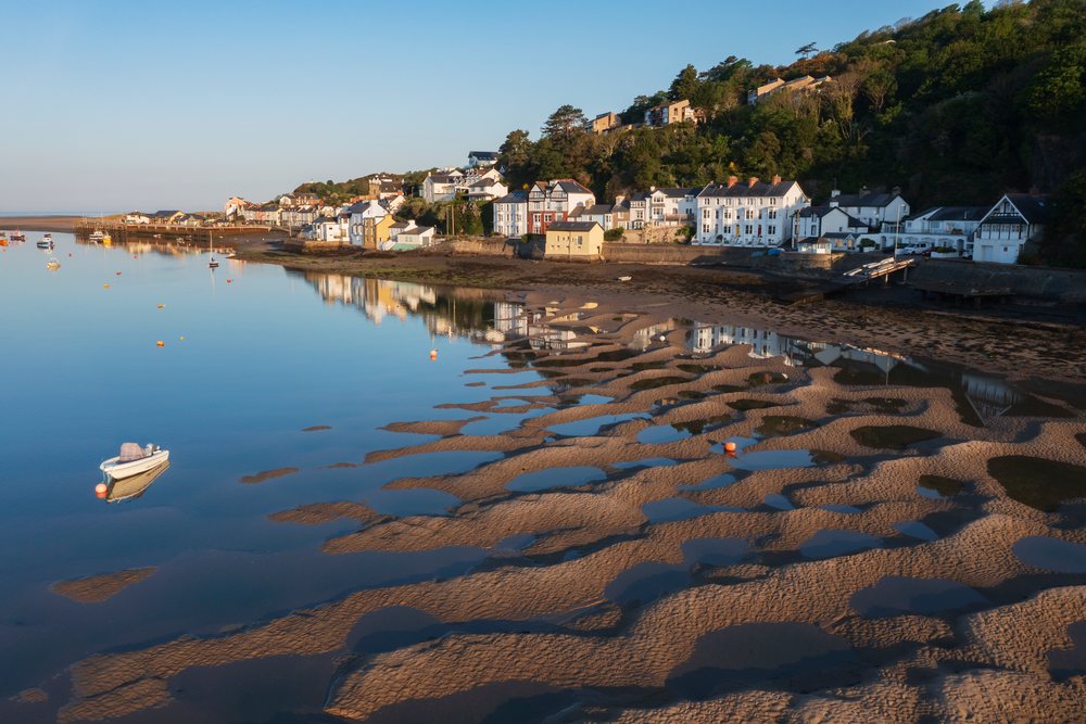 Calm Dyfi estuary with tidal sand and mud patterns, boats floating on water, and coastal houses in Ynyslas, Landscape, Aberdyfi, Gwynedd, Wales.