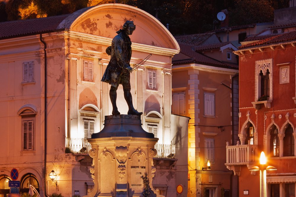 Statue of Giuseppe Tartini holding a violin bow illuminated in the evening town square, Piran, Slovenia.