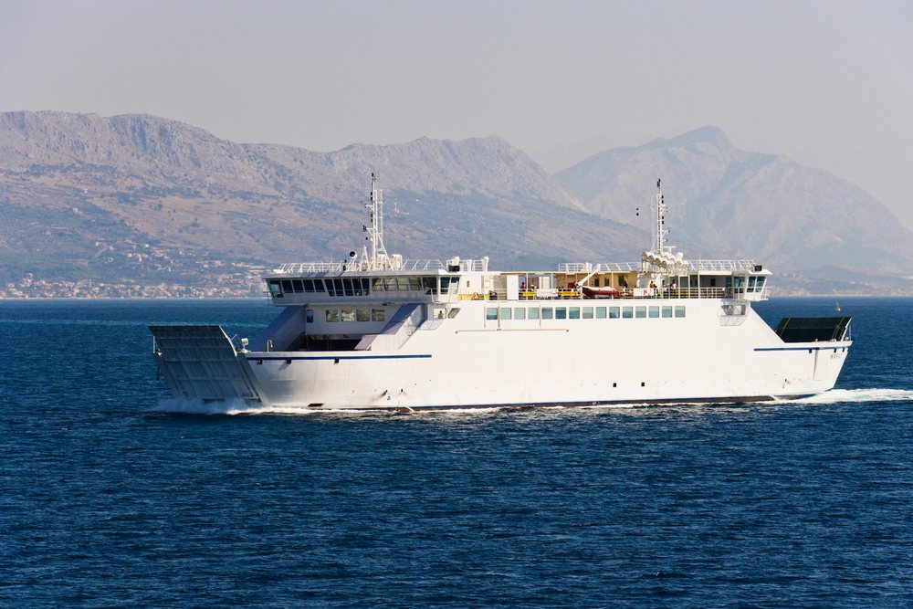 Ferry crosses the calm Adriatic Sea with a mountainous Croatian coastline visible in the background under a clear sky.