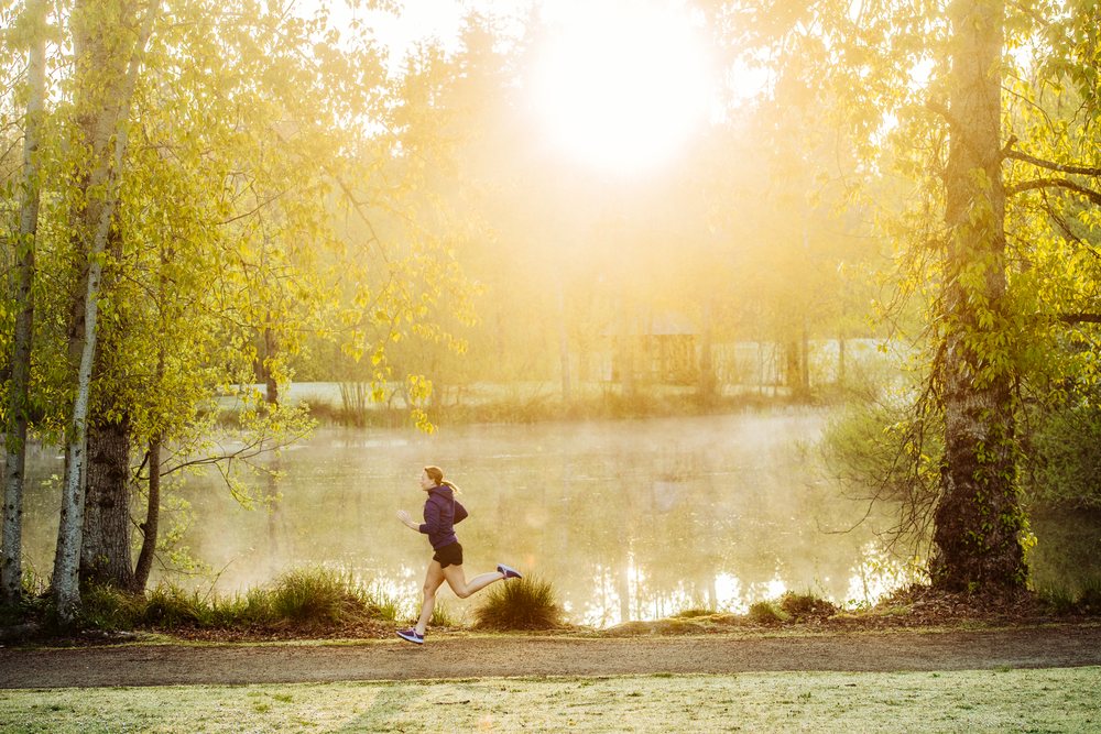 Woman running on a dirt trail in a misty morning park with sunlight filtering through trees, Washington, Bainbridge Island, USA.