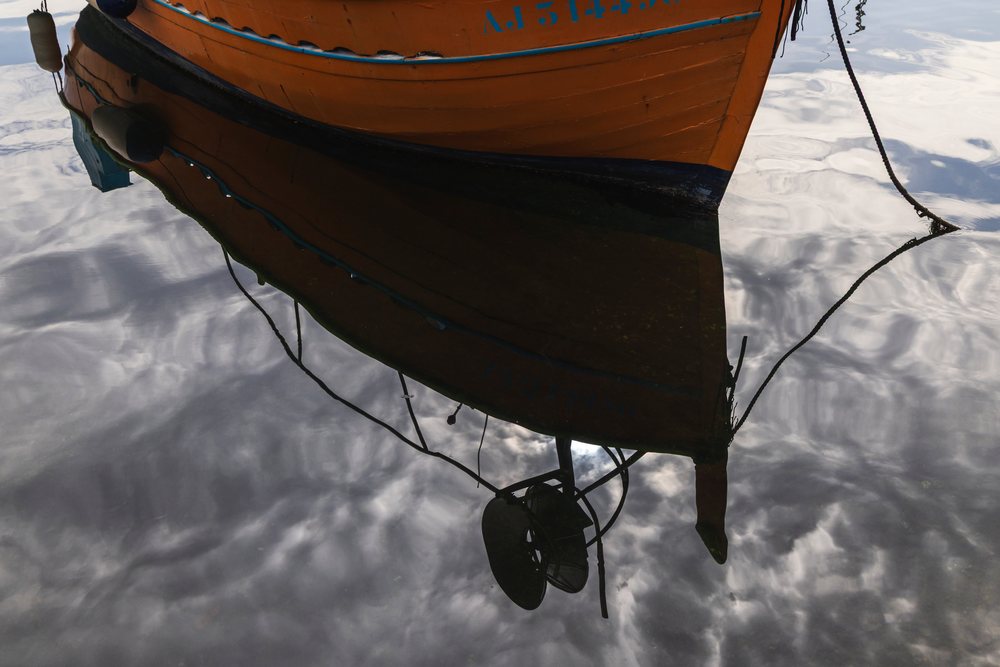 Orange Fishing Boat hull moored with ropes reflected in the calm water, Travel Photography, Ajaccio, Corsica, France.