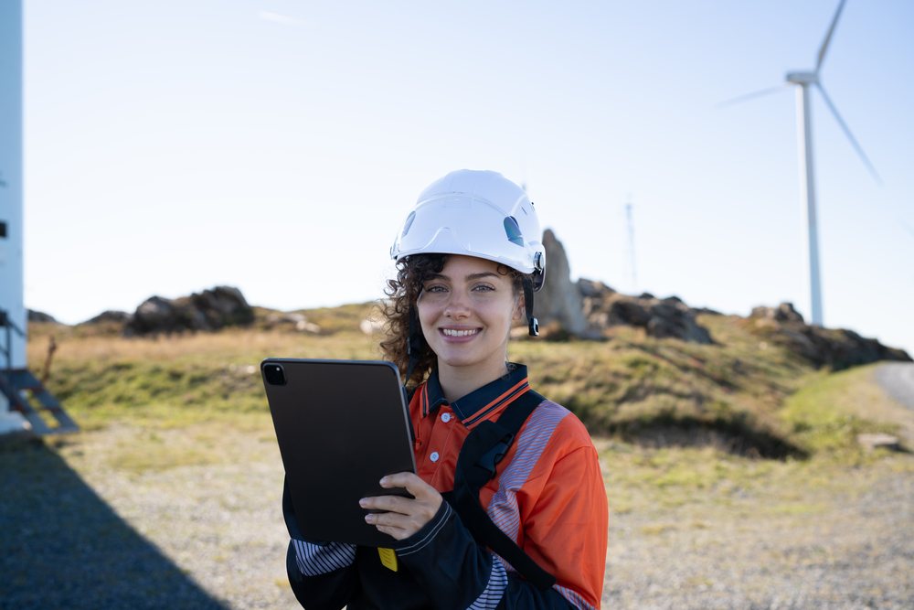 Female engineer wearing safety helmet and high visibility clothing holding a tablet at a wind farm, outdoors during daylight, sustainability, renewable energy, Galicia, Spain.