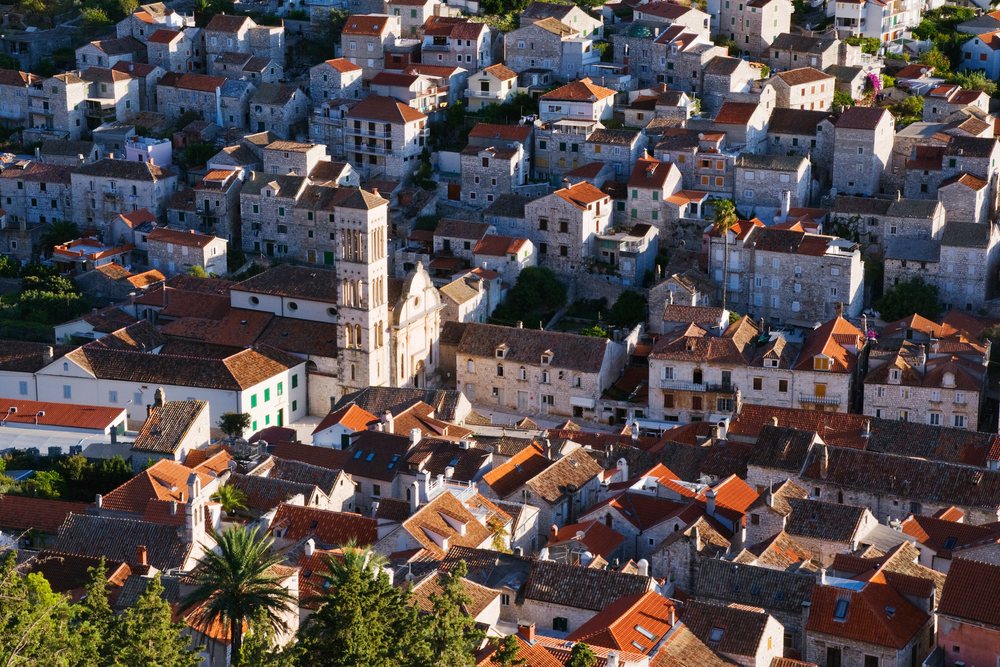 Sunlit town of Hvar featuring historic stone buildings and red tile roofs with a church tower and Mediterranean trees, Croatia.