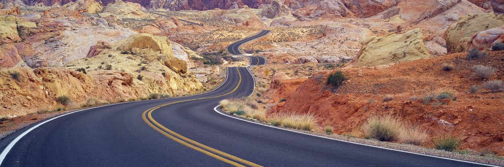 Winding paved road passes through a colorful rocky desert landscape with dry shrubs, Nevada, USA.