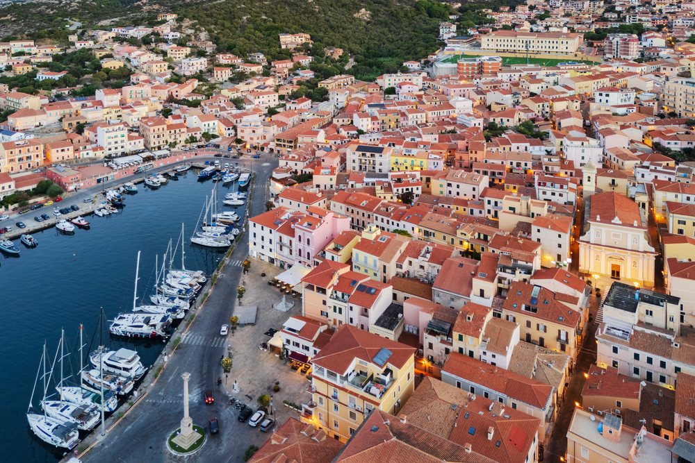 Aerial view showcasing boats docked in the harbor and red tile roofs of La Maddalena, alongside its waterfront and church tower, Travel Images, Sardinia, Italy.