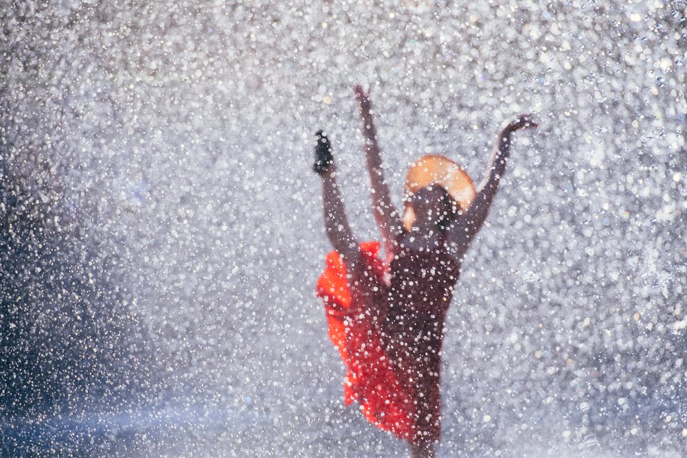 Person dancing joyfully outdoors in a red dress and hat, USA.