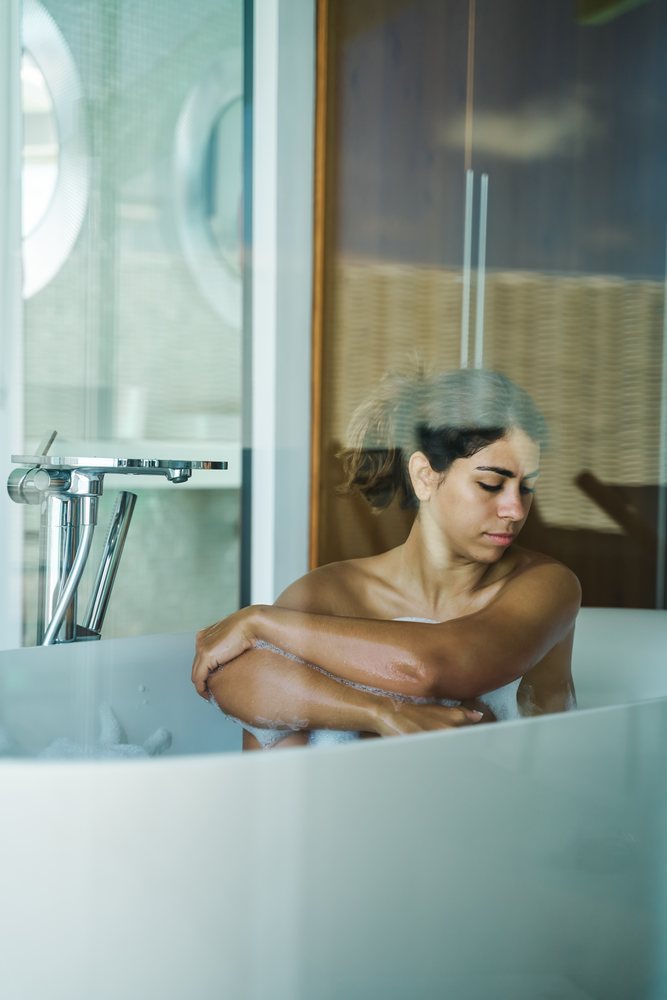 A young woman relaxes in a bathtub with soapy water in a modern bathroom in the, Maldives.