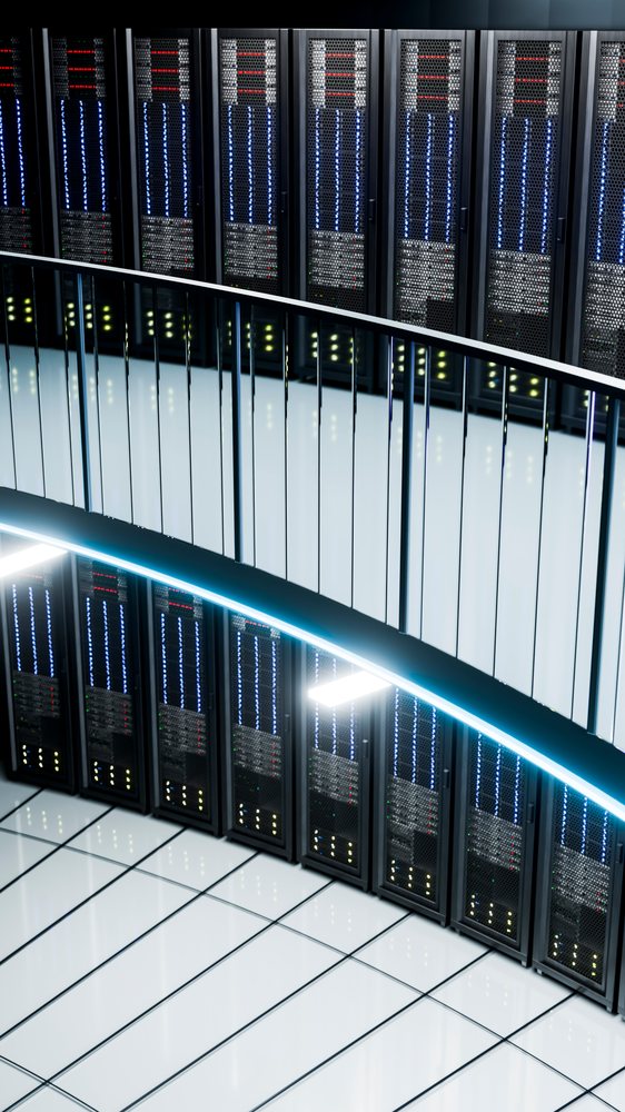 Rows of black server racks with blue, red, and yellow indicator lights behind a curved white railing in a modern data center.