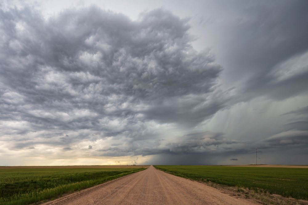 Dirt Farm Road extends beneath a dark supercell thunderstorm over open grassy fields, Storm Chasing, Kimball, Wyoming, USA.