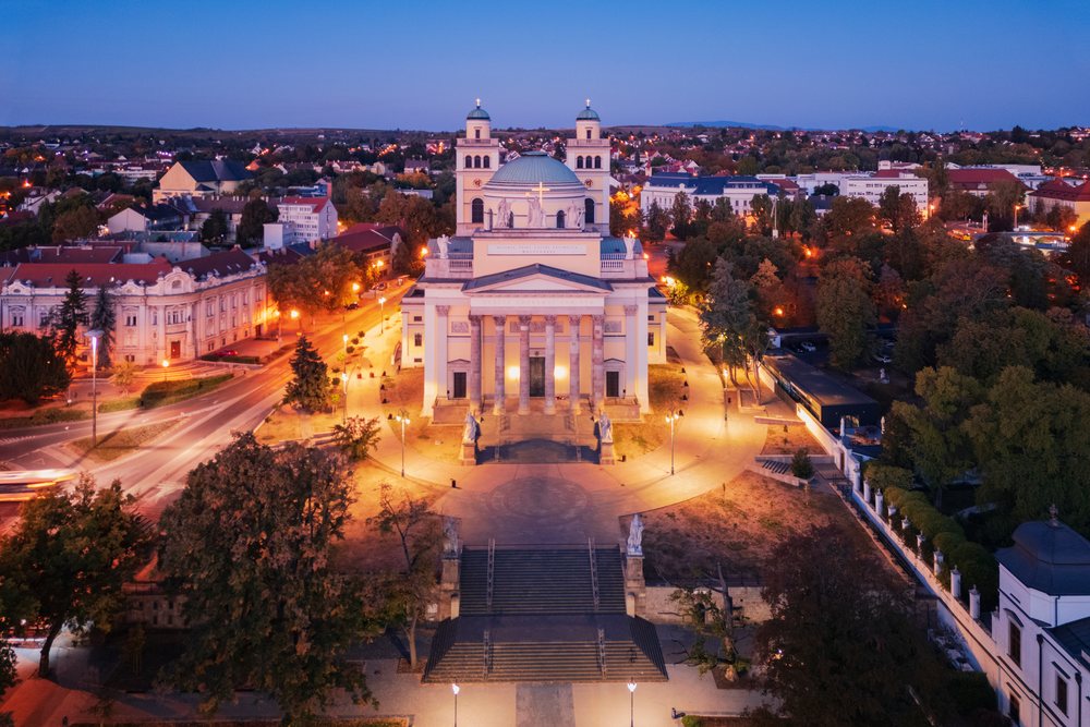 Cathedral basilica of St John the Apostle illuminated at Dawn in the cityscape of Eger with surrounding buildings, streets, and street lamps visible, Hungary.