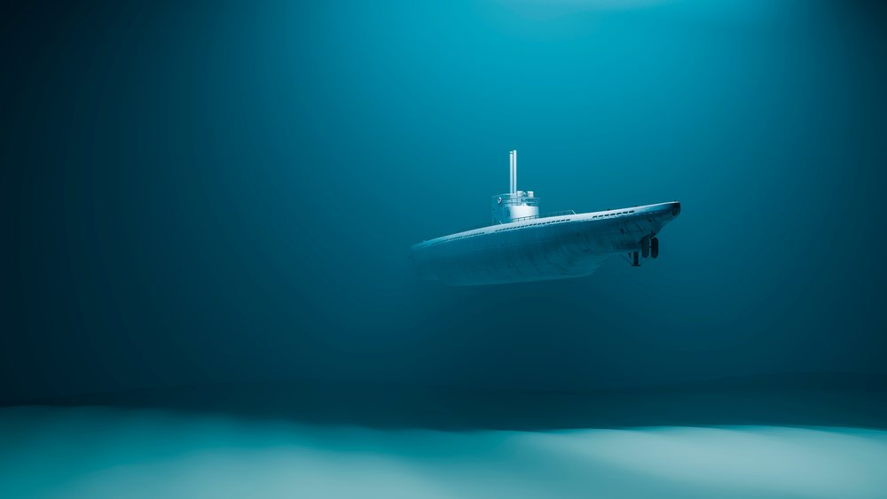 Submarine cruising underwater in the deep ocean with visible clear water and sandy sea floor below.