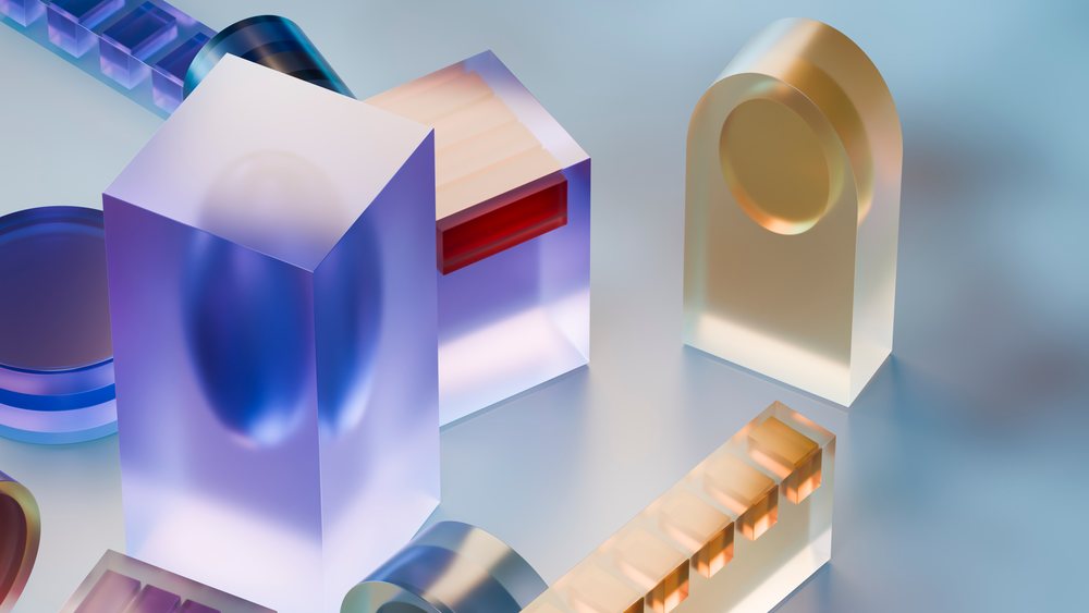 Abstract colorful translucent geometric shapes are arranged on a smooth reflective surface with soft lighting and shadows.