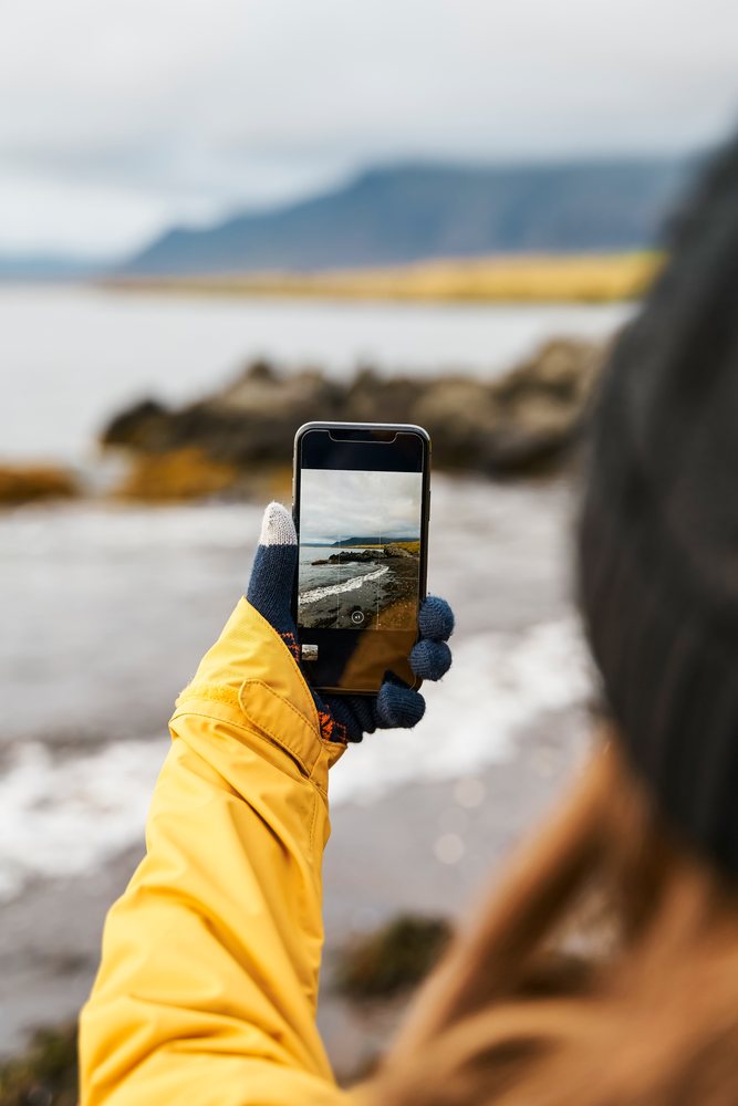 White Person in yellow jacket takes photo of rocky coast