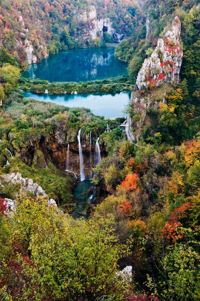 Waterfalls cascade over limestone cliffs surrounded by autumn foliage and a lake, Plitvice Lakes National Park, Croatia.