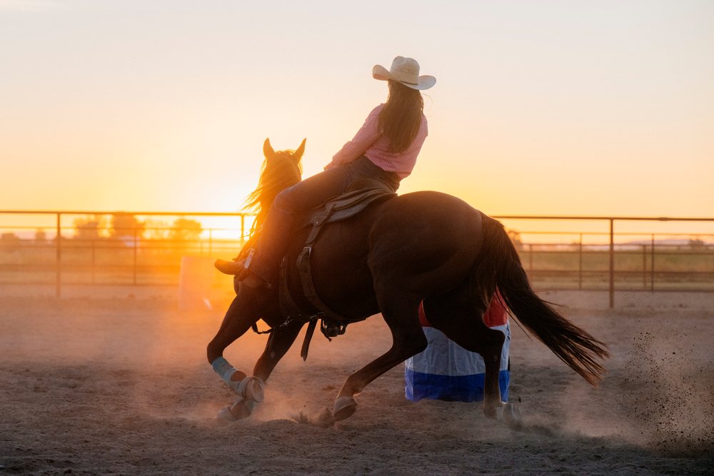 Cowgirl on horseback performs Western riding in a dusty arena at sunset, Southwest USA.