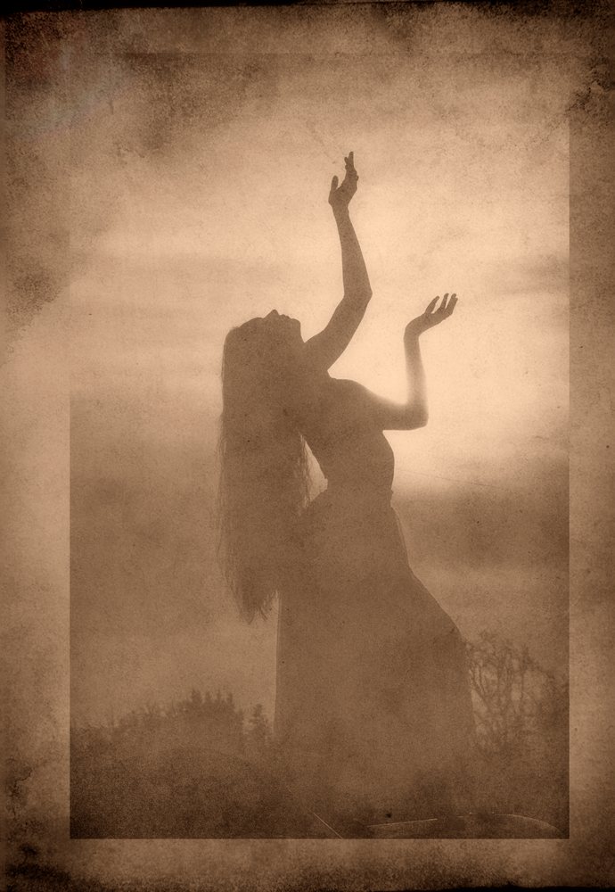 Silhouette of a woman dancing outdoors with arms raised at sunset in sepia tone, USA.