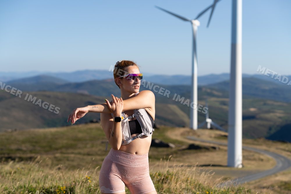 A white woman stretches during an outdoor workout near wind turbines