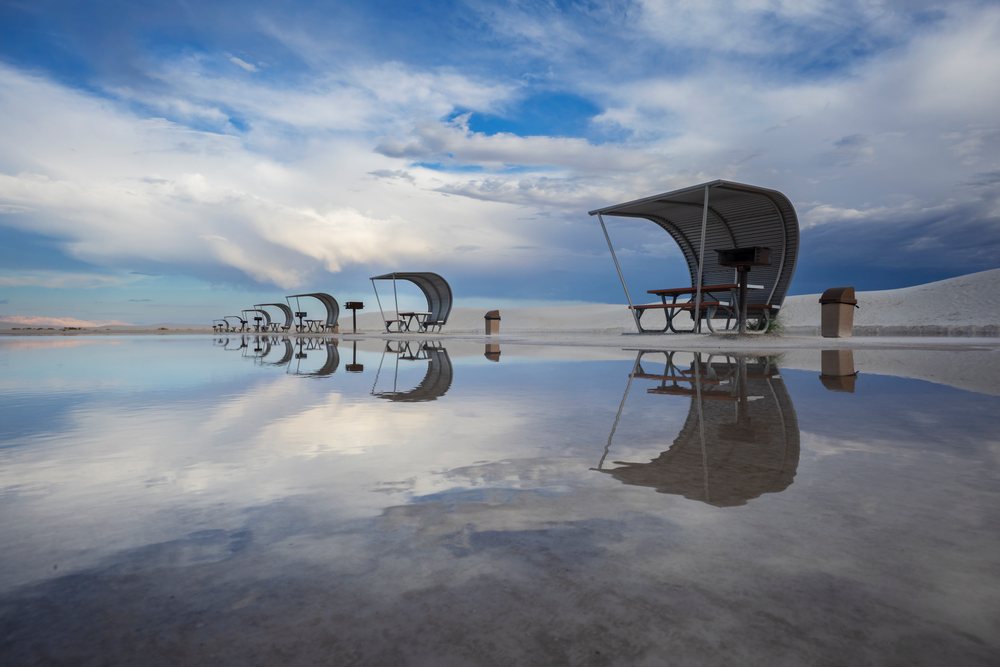 Reflection of metal shelters with picnic tables, grills, and trash bins on water at white Sands National Monument, Landscape, Wildlife, Alamogordo, New Mexico, USA.