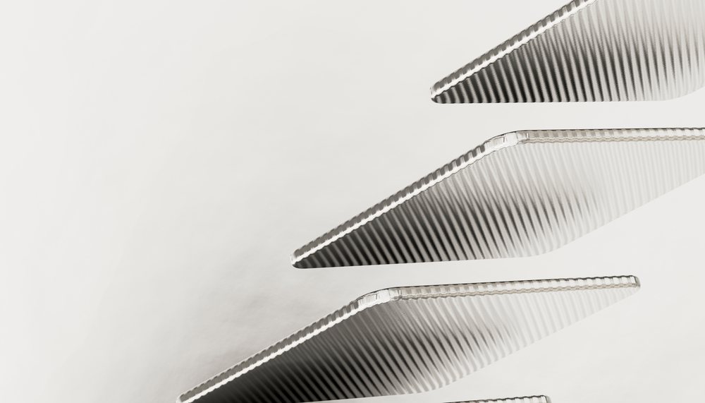 Close-up of parallel metallic triangular objects with rippled textured surfaces arranged diagonally on a monochrome background under studio lighting.