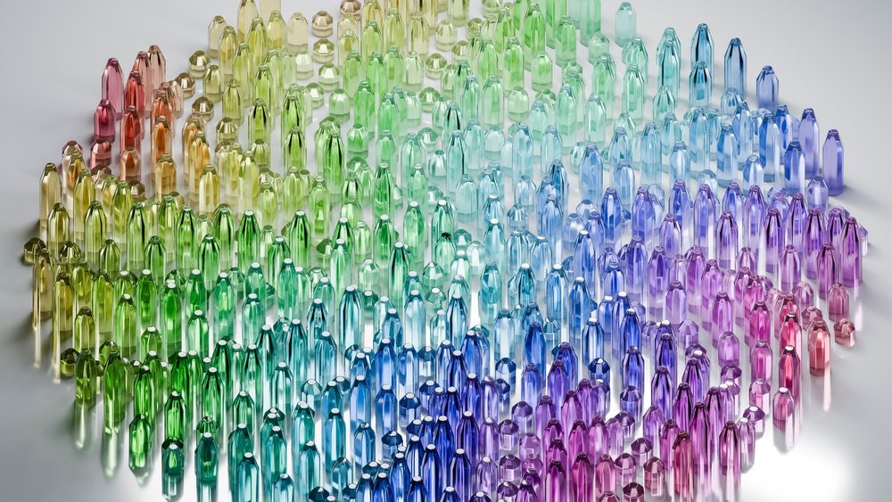 Faceted transparent crystals arranged in a spiral pattern displaying a rainbow color gradient on a reflective surface.