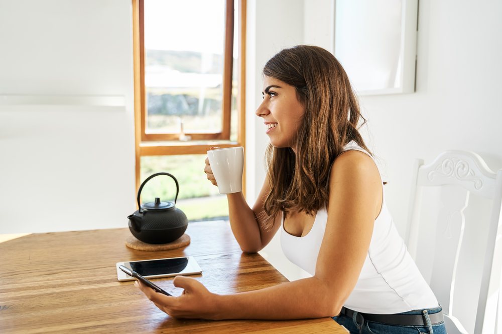 A white woman drinking tea and using her smartphone