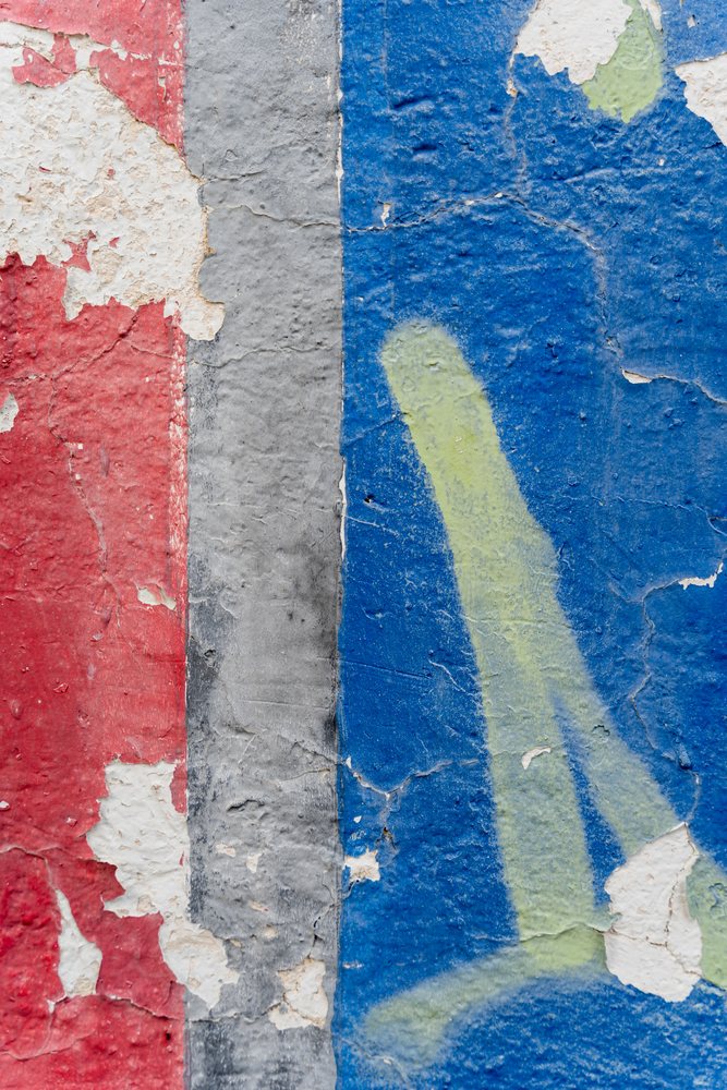Peeling layered paint on a weathered wall surface showing red, gray, blue, and yellow colors, texture, abstract texture, background, wallpaper, Spain.