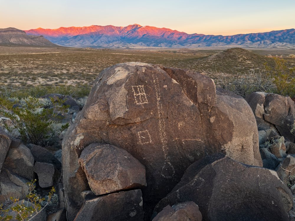 Petroglyphs carved on a large boulder at three Rivers Petroglyph Site with Sunset-illuminated mountains in New Mexico desert, landscape, wildlife, USA.