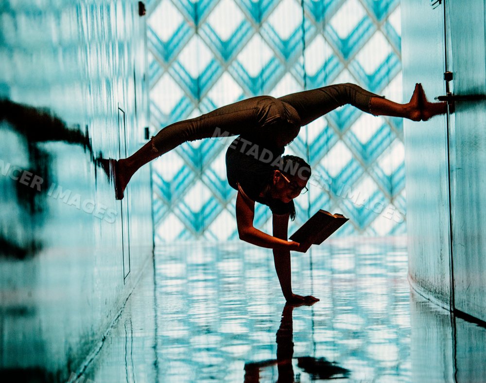 A woman performs a handstand reading a book in a library
