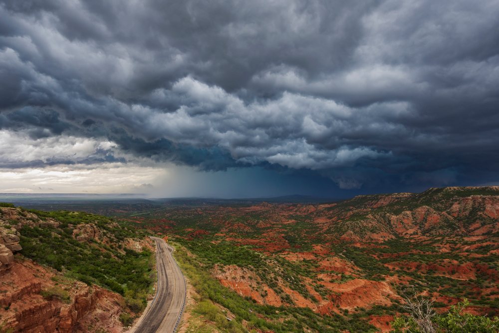 Storm clouds and a rain shaft loom over the red rocky terrain of Palo Duro Canyon with a winding road, Claude, Texas, USA.