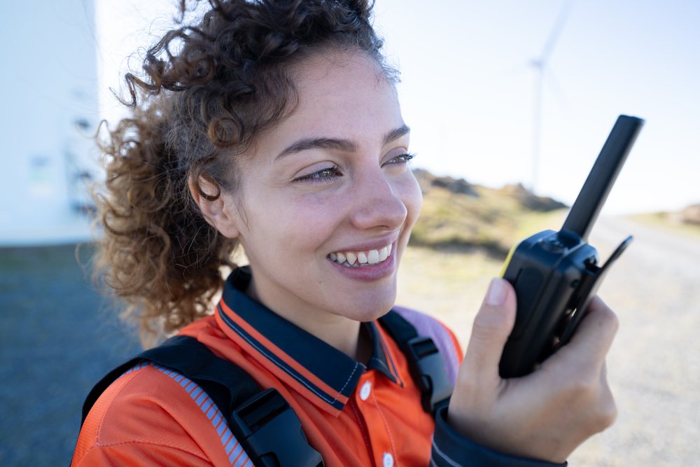 Woman in safety wear communicates using a walkie talkie outdoors near a wind turbine in rural, sustainability, renewable energy, Galicia, Spain.