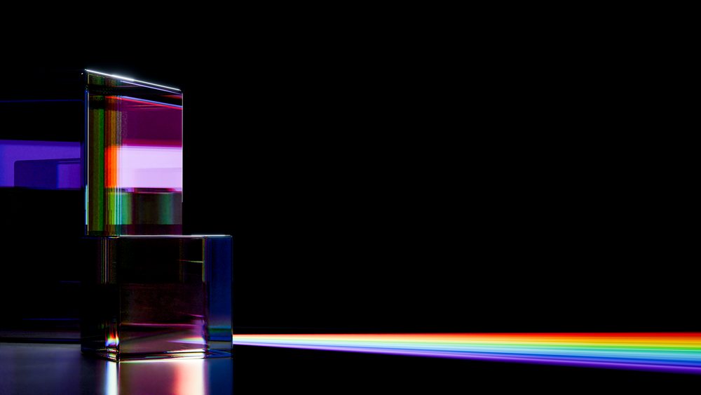 Light refracted through a transparent glass prism emits a vivid rainbow spectrum against a dark background.