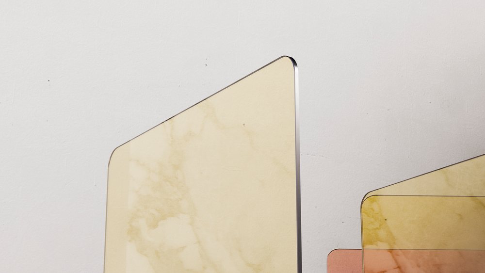Colored glass panels with rounded corners in beige, yellow, and orange shades overlapping against a white wall background in a studio setting.