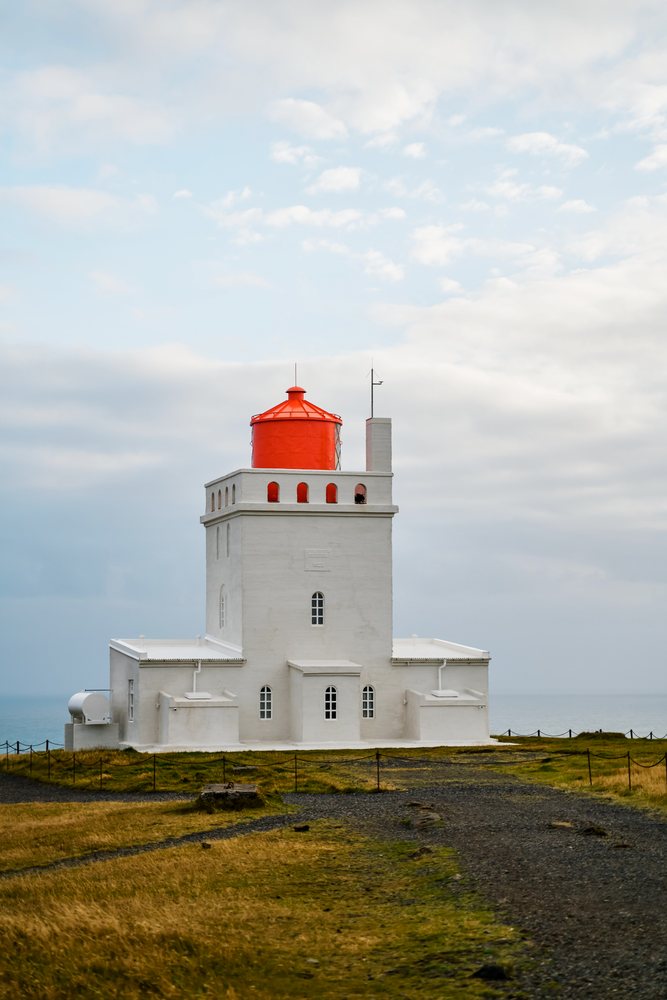 A white lighthouse with a red roof on the coast of Iceland