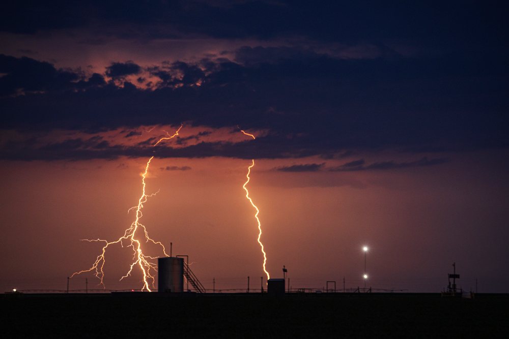 Lightning strikes illuminate Farm Fields and a metal tank under a dark stormy night sky, in Tornado Alley of the Great Plains, Storm Chasing, Weather, Environmental issues, Perryton, Texas, USA.