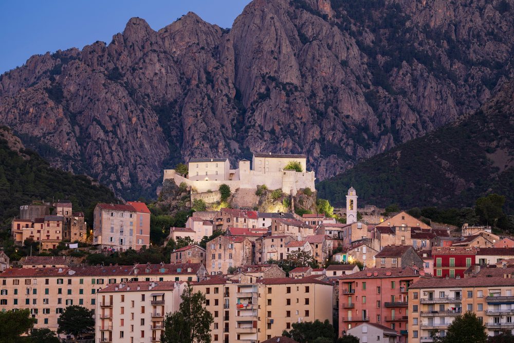 Fortress illuminated on a hilltop overlooking the town of Corte at Dawn with rocky mountains and vegetation nearby, Travel Photography, Corsica, France.