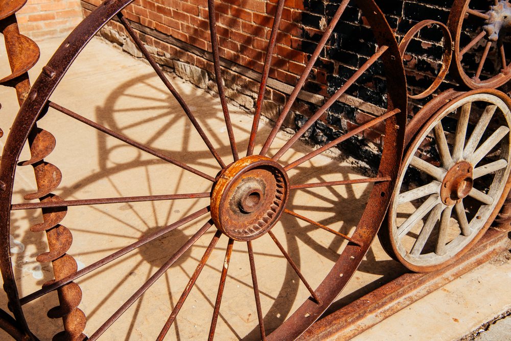 Rusty iron wheels with spokes cast shadows on concrete near a brick wall, fall colors, Durango, Colorado, USA.
