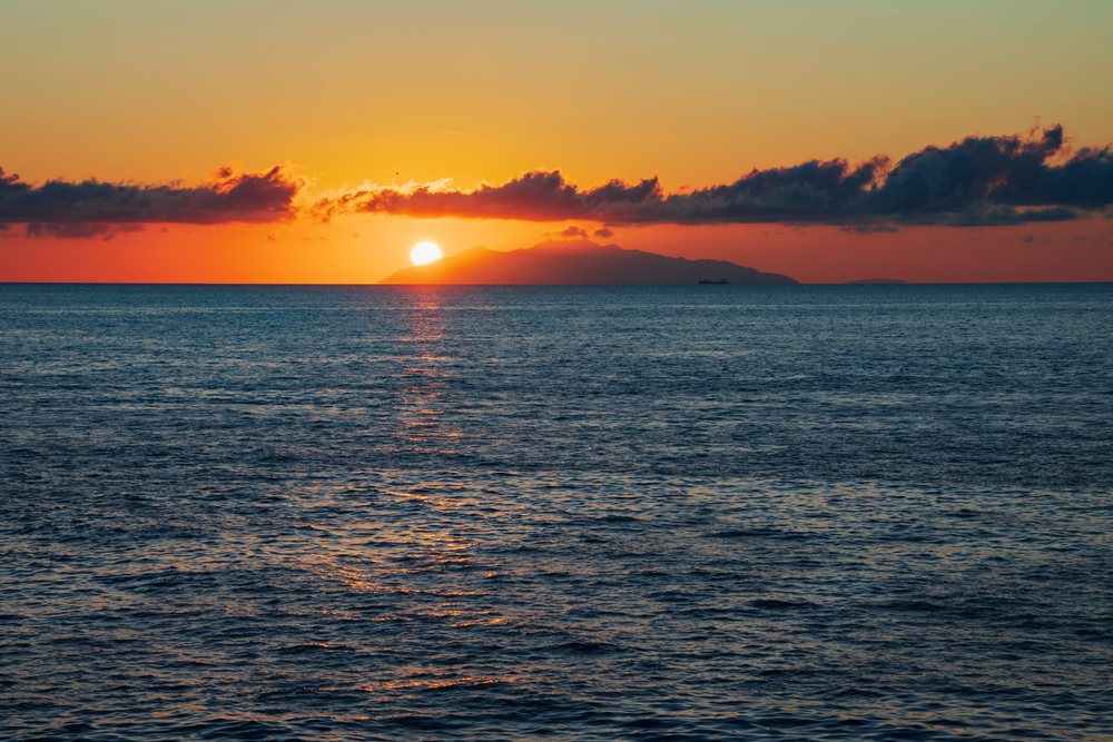 Sunrise near the horizon over the Isle of Elba with calm sea water and scattered clouds off the coast of, Travel Photography, Bastia, Corsica, France.