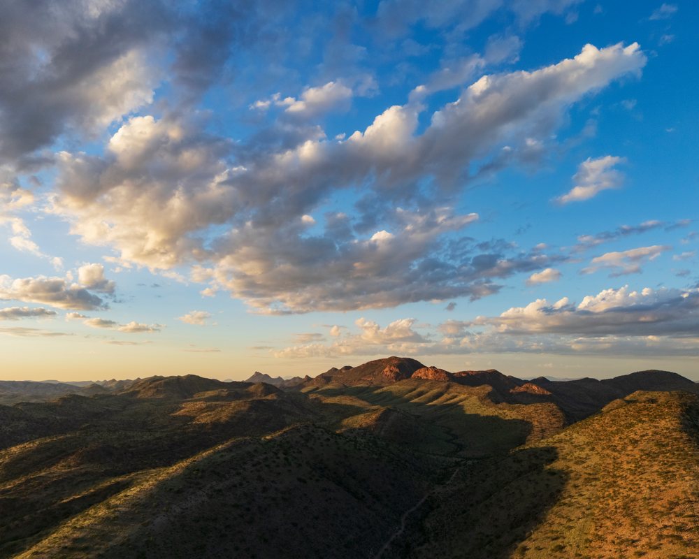 Mountain and valley landscape with clouds and sunlight over terrain and vegetation, Etambura, Kunene Region, Namibia.