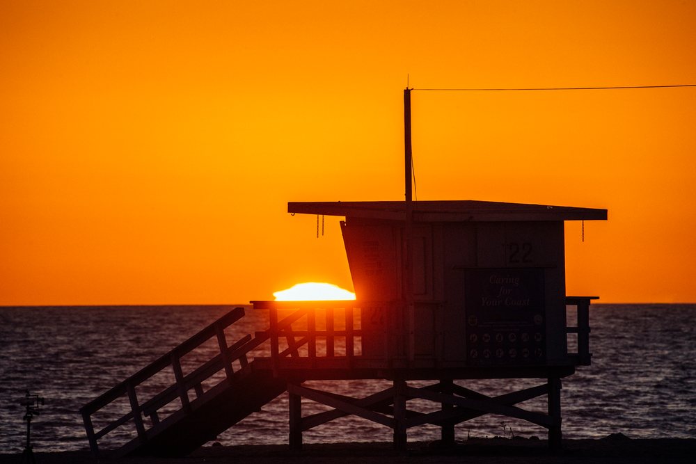 Silhouetted lifeguard tower with stairs and railings on a beach at sunset with ocean water and orange sky, Santa Monica, CA, USA.