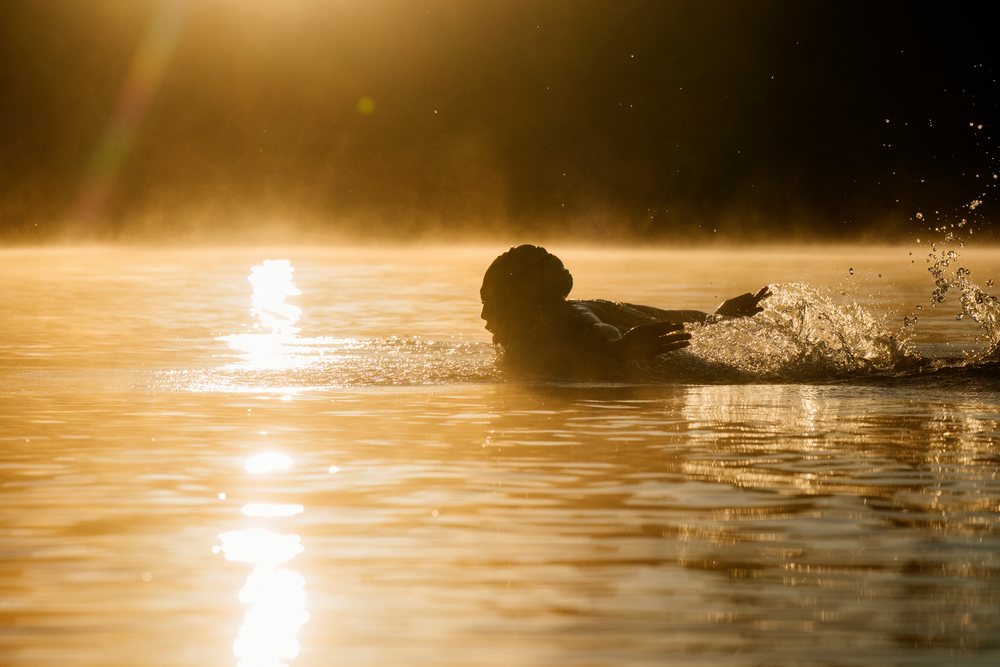 Person swimming in a calm lake with sunlight reflecting off the water surface, USA.