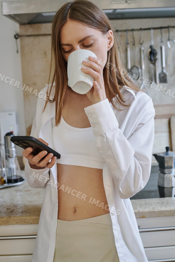 A young white woman drinks coffee and texts on her smartphone
