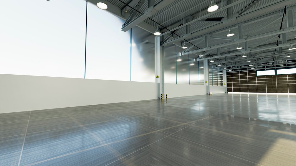 Empty industrial warehouse interior with large windows, high ceiling, metal beams, overhead lights, and concrete floor suitable for car manufacturing or industrial use.