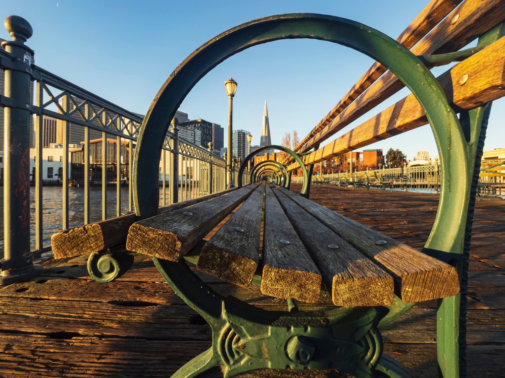 Wooden Bench with green metal supports on Pier 7 at sunrise overlooking San Francisco waterfront with Transamerica Pyramid in the background, landscape, cityscape, city life, California, USA.