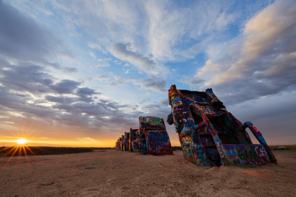 Colorfully graffitied Cadillac car sculptures buried nose-down at Cadillac Ranch, under a cloudy Sunrise sky, Storm Chasing, Amarillo, Texas, USA.