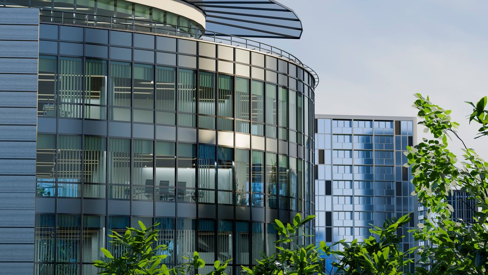 Modern office building with glass facade showing a conference room interior behind green foliage in an urban business district.