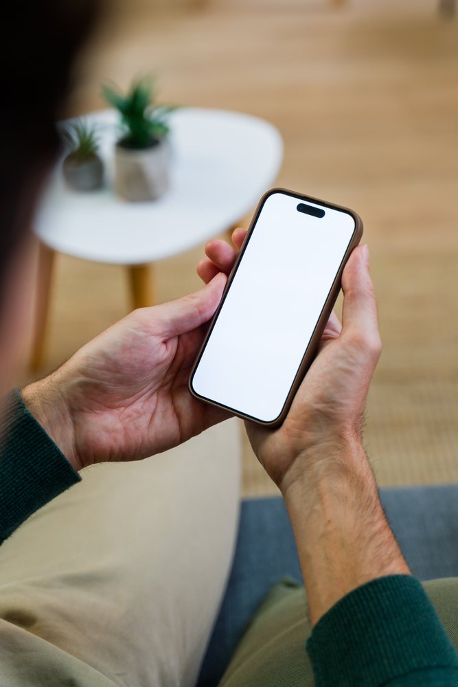 Person holding smartphone with blank screen indoors near a table with small plants, Spain.