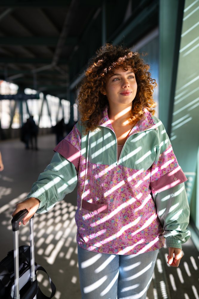 Woman with curly hair pulling a suitcase walks through a sunlit interior corridor, Spain.