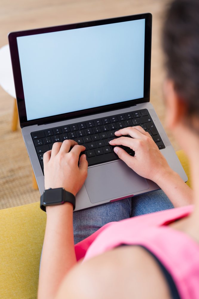A person in a pink top types on a laptop with a blank screen while sitting indoors, Spain.