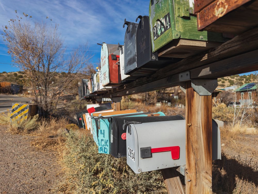 Row of rural Mailboxes mounted on wooden posts along a roadside, USA under a blue sky, Americana, Historic, Madrid, New Mexico.